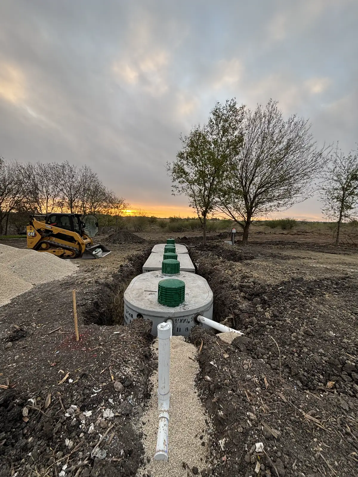 Row of newly installed septic tanks in an open trench at sunset on a Central Texas jobsite